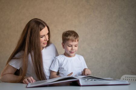 A middle-aged Caucasian woman hugs a little son and shows a photo album. A little boy sits on his mothers lap and looks at old photographs. Pleasant memories. Close family relationships.の写真素材