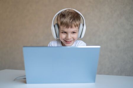 Cute little boy is watching cartoons or a movie on a laptop. Caucasian child sits at a table at home...