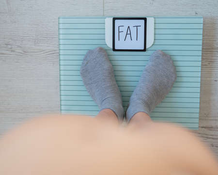 Top view of womens feet in gray socks on a floor scale. The inscription on the screen is fat. An obese man measures his weight. Naked big belly.の写真素材