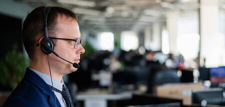 Portrait of a male call center operator in headset at workplace. A man works in an open space office...