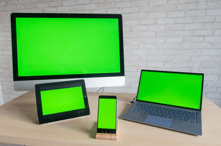 On the table are a computer laptop digital tablet and a phone with green screens on a brick wall background. Devices with blank screens.のeditorial素材