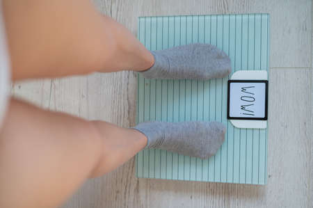 Top view of womens feet in gray socks on a floor scale. The inscription on the screen wow. An obese woman measures her weight. Girl with a perfect flat stomach.の写真素材