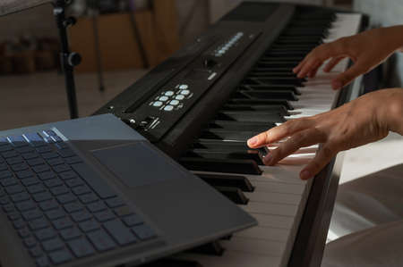 Closeup of female hands on an electronic piano. A laptop on a keyboard instrument. Online lesson....