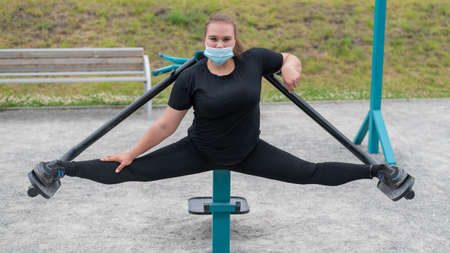 Overweight young woman in a protective mask is training on the sports ground. An obese girl is...