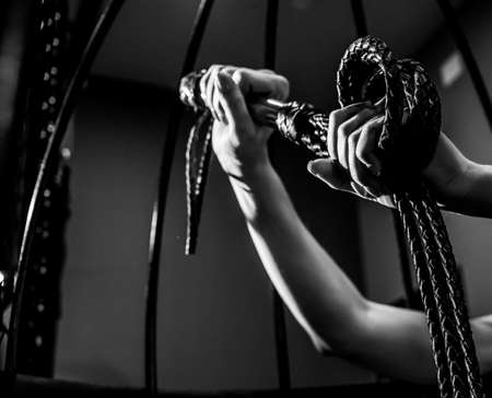 Female hand with a long woven leather lash in a cage. BDSM Punishment and pleasure. Cropped.