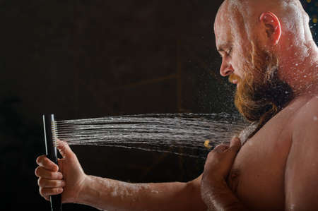 Male takes a shower. A brutal man with a red beard is standing in the bathroom under running water...