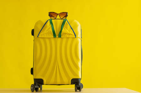 Yellow suitcase on wheels with tiger sunglasses and a mini bikini on a yellow background in the studio. Set for a beach vacation. Copy space. No people. Summer vacation at sea.の写真素材