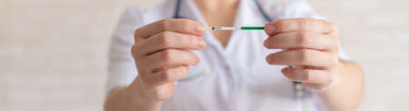 A faceless female doctor holds a negative quick pregnancy test. Gynecologist in a medical coat and with a stethoscope. Problems conceiving a baby.の写真素材