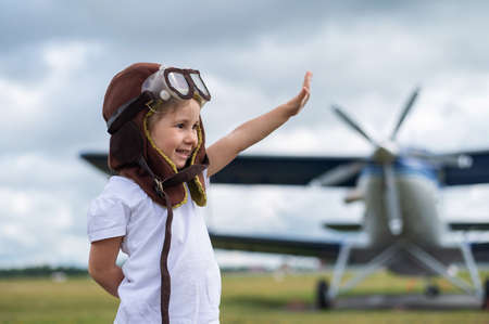 A cute little girl dressed in a cap and glasses of a pilot on the background of an airplane. The child dreams of becoming a pilot.の写真素材