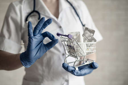 A faceless female pharmacist holds a mini shopping cart with medications and gestures with the ok. Taking vitamins is the key to good health. Doctors recommendations.の写真素材