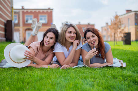 Three beautiful Caucasian young women lie on the lawn in the countryside. The blonde brunette and...