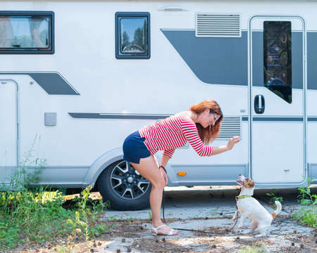 Beautiful caucasian woman is training a dog next to the motorhome. Travel with your pet in a mobile...