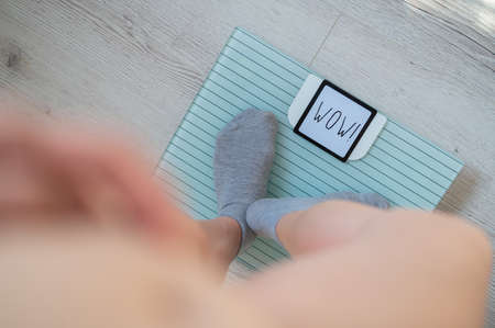 Top view of female legs in gray socks on electronic scales. The inscription on the display is wow.
