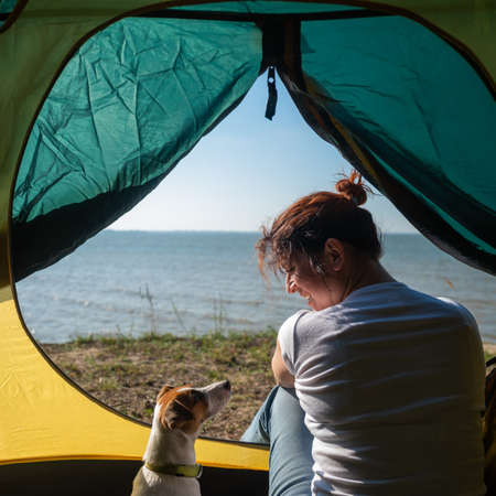 A woman and a dog are sitting in a tourist tent by the sea. Recreation in nature.の写真素材
