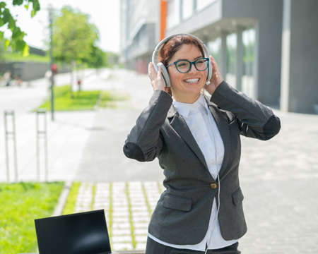 Caucasian business woman in a suit listening to music with headphones and singing along to dance outdoorsの写真素材