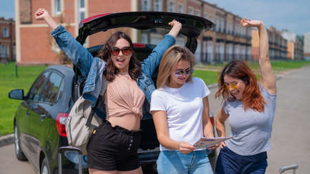 Three friends are going on a road trip for the summer vacation and are looking at the map. Young...
