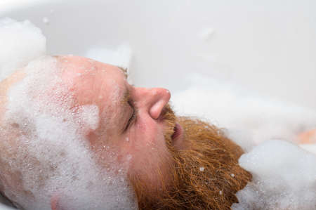 Close-up portrait of funny red-bearded bald man taking a bath with foamの写真素材