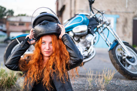 A red-haired woman puts on a helmet for safe motorcycle riding.