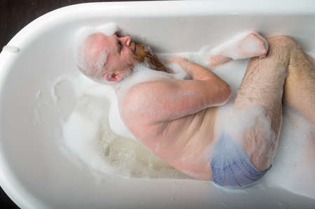 Top view of a bald man with a red beard splashing in the foam bath. Humorous photo. A parody of...