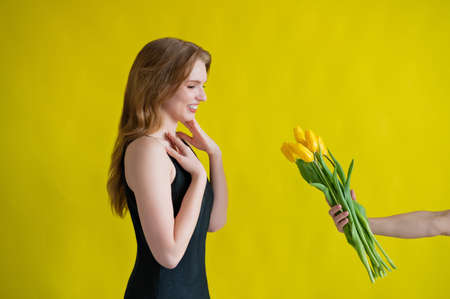 Caucasian woman accepts tulips as a gift on yellow background.の写真素材