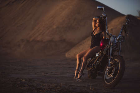 Beautiful sexy woman in lace bodysuit and high heels sits on a motorcycle on an industrial backgroundの写真素材