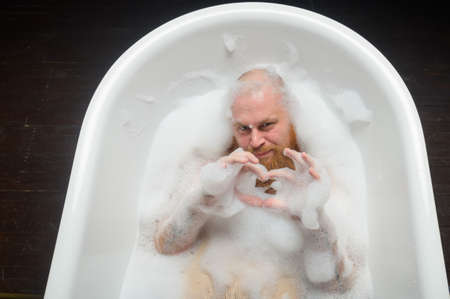Top view of a bald man with a red beard splashing in the foam bath. Humorous photo. A parody of glamorous girls.の写真素材