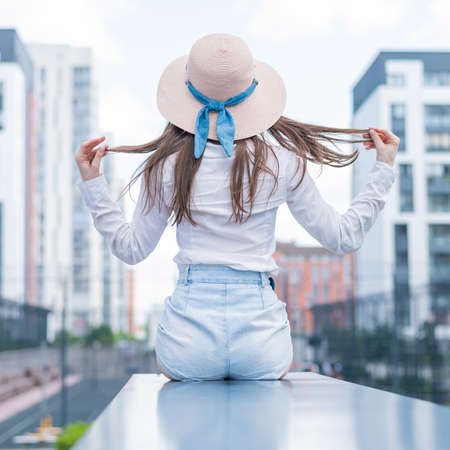 Rear view of a woman in a hat sitting on the background of the cityの写真素材
