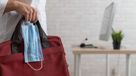 Close-up of female hands with a briefcase and a medical maskの写真素材