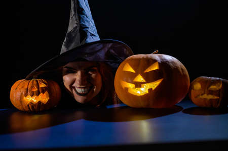 The head of an evil witch is on the table next to the glowing pumpkin jack-o-lanternの写真素材