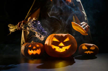 Witch casts a spell on a steaming pumpkin in the dark on Halloweenの写真素材