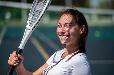 Beautiful smiling woman with a shadow from a tennis racket on her face on a sunny dayの写真素材