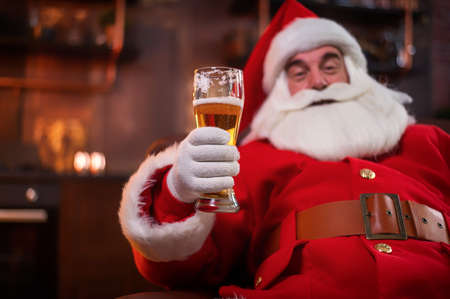 Santa Claus drinks beer while sitting in a leather armchairの写真素材