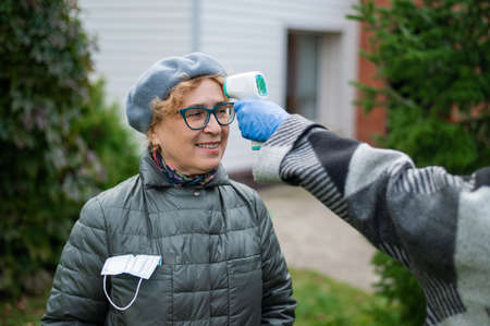 The doctor measures the temperature of an elderly woman with a non-contact infrared thermometer outdoorsの写真素材