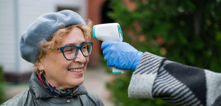 The doctor measures the temperature of an elderly woman with a non-contact infrared thermometer outdoorsの写真素材