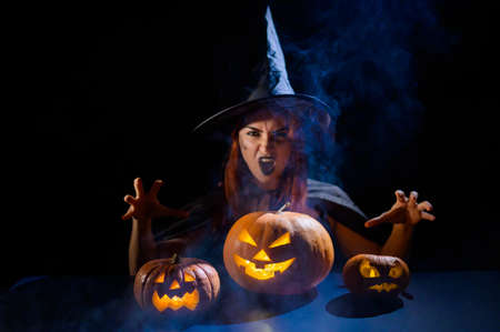 The evil witch casts a spell on pumpkins. Portrait of a woman in a carnival halloween costume in the darkの写真素材