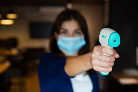 A female office worker in a mask holds a contactless electronic thermometer