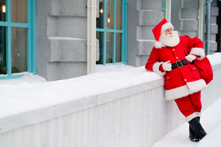 Pensive santa claus is leaning against the facade of a house in winterの写真素材
