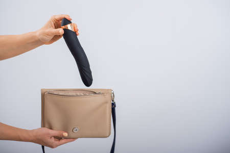 A woman puts a dildo in a handbag on a white background. Close-up of female hands with a black vibratorの写真素材