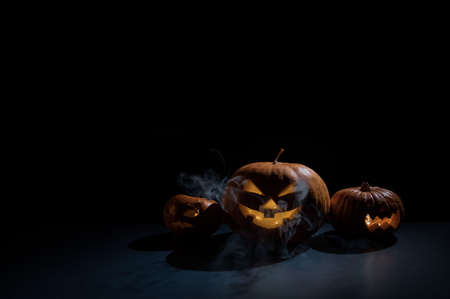 Halloween card. jack o lantern with candles glow on a black background. A row of creepy pumpkins with carved grimaces smokes in the dark.の写真素材