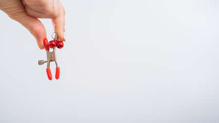 Close up womans hand holding nipple clamps on a white background. BDSM sex toyの写真素材