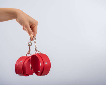Red leather handcuffs in female hands on a white background. BDSM accessories