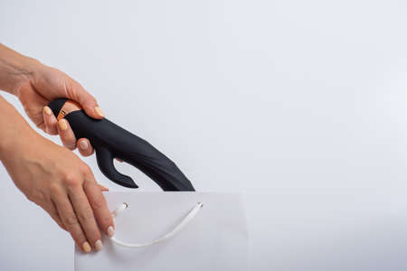 A woman makes a purchase and puts a dildo in a bag on a white background. Close-up of female hands with a black vibratorの写真素材