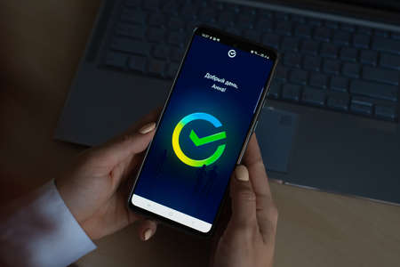 October 18, 2020 Russia, Novosibirsk: Sbermarket logo on a smartphone. A woman orders food to a...