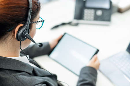 A business woman with a headset holds a digital tablet while sitting at a deskの写真素材