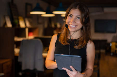 Beautiful business woman wearing in a headset is holding a digital tablet in the office.