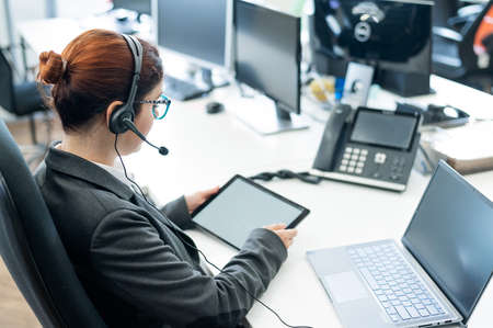 A business woman with a headset holds a digital tablet while sitting at a deskの写真素材