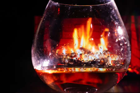 Close-up on a glass of brandy in the dark on the background of the fireplace.の写真素材