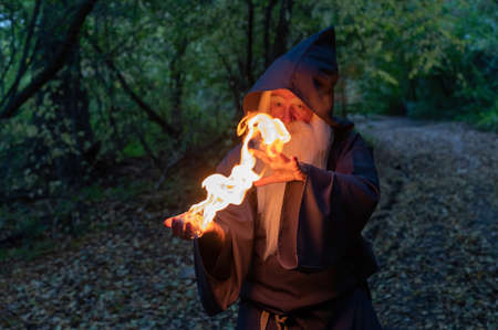 An elderly gray-haired witcher casts a fire spell in the forest. Man in wizard costumeの写真素材