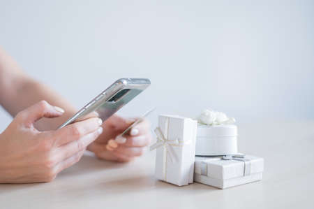 A faceless woman sits at a table and holds a mobile and a credit card in her hands. Online shopping for gifts conceptの写真素材