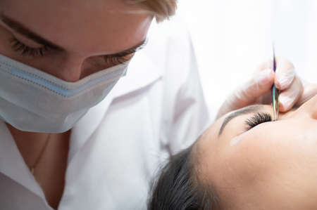 Close-up of a beautiful asian woman on eyelash extension procedure. Double volume false eyelashes. Lashmaker at work.の写真素材
